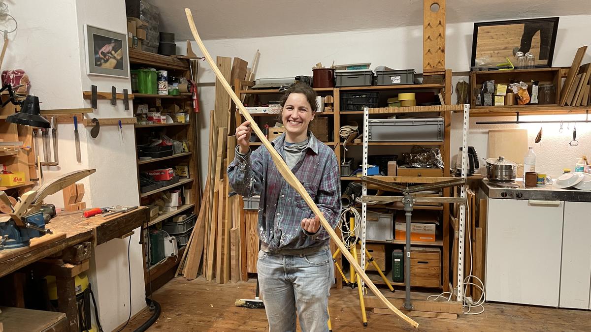 Eine Frau hält in der Werkstatt einen frisch gebauten Langbogen