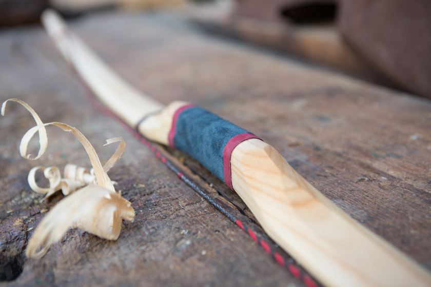 Handgebauter Holzbogen mit Lederwicklung, daneben frische Hobelspäne